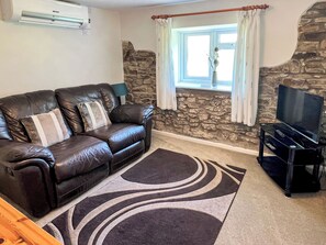 A living room with a leather sofa, a flat-screen TV, a stone wall, and a window with curtains.