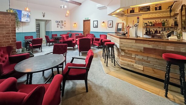 Eine Bar mit Holztresen und Hockern, umgeben von roten Sitzmöglichkeiten aus Stoff und Tischen.