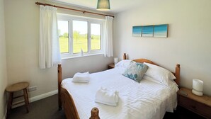 A bedroom with a bed, a window with curtains, a bedside table, and a nightstand. - Willow Apartment - UK49303 (Woolfardisworthy, Clovelly)