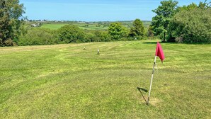 Ein Golfplatz mit roter Fahne, grünem Rasen, Bäumen und Gebäuden in der Ferne.