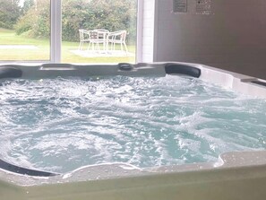 Un bain à remous avec vue sur une zone verdoyante et une chaise blanche installée à l’extérieur.