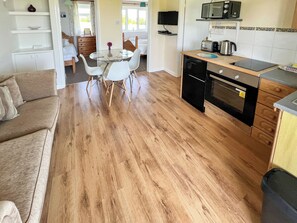 Eine moderne Küche mit Mikrowelle, Toaster und Wasserkocher, ein Essbereich mit Glastisch und Stühlen sowie ein Holzboden.