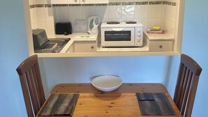 A compact kitchen with a microwave, toaster, and kettle, a small sink, and a dining table with two chairs. - Hawfinch Apartment - UK49304 (Woolfardisworthy, Clovelly)