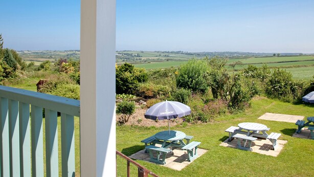 Un balcon avec vue sur un paysage verdoyant, un espace salon extérieur et une table de pique-nique.