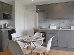 Una cocina moderna con una mesa de comedor de vidrio, sillas blancas, electrodomésticos de acero inoxidable y armarios grises.