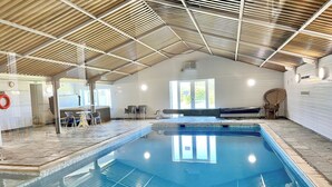Une piscine intérieure avec un sol carrelé, un plafond en bois et un espace détente avec des chaises.