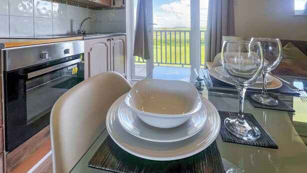Un espace repas avec une table en verre, des chaises blanches et une vue sur l’extérieur.