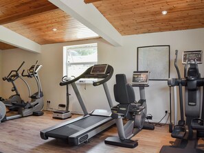 Een fitnessruimte met loopbanden, elliptische trainers en een hometrainer, met houten plafonds en een raam.