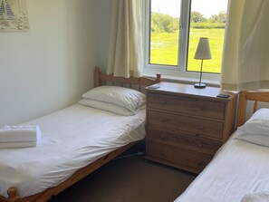 A bedroom with two beds, a wooden dresser, a lamp, and a window with a view of a green landscape.