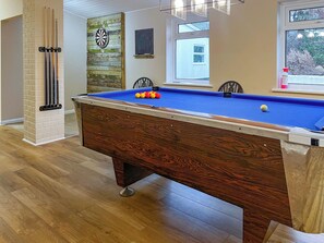 A pool table with balls, a dartboard, and a chalkboard in a room with wooden flooring and a window.