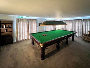 Een pooltafel in een ruimte met een nooduitgang, gordijnen en een stoel.