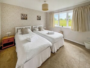 Une chambre avec deux lits, une table de chevet, une fenêtre avec des rideaux et un mur orné d’un motif floral.