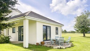 A single-story house with a covered patio, a lawn, and a large window. - Jasmine Apartment - UK49309 (Woolfardisworthy, Clovelly)