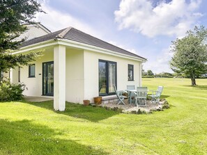 Ein eingeschossiges Haus mit überdachter Terrasse, Rasenfläche und großem Fenster.