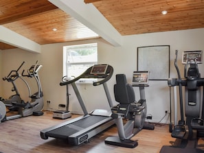 Ein Fitnessraum mit Laufbändern, Crosstrainern und einem Ergometer, ausgestattet mit Holzbalkendecken und einem Fenster.