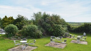 Een terras met metalen stoelen en tafels, omgeven door weelderige begroeiing en uitzicht op het landschap.