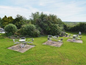 Un espacio de estar al aire libre con sillas y mesas de metal, rodeado de exuberante vegetación y vistas al campo.