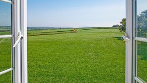 Uitzicht door een raam op een groen veld met heuvels in de verte.