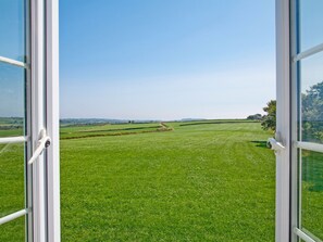 Vista a través de una ventana de un campo verde con colinas al fondo.