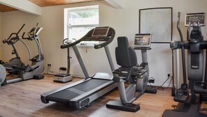 Een fitnessruimte met loopbanden, elliptische trainers en een hometrainer, met houten plafonds en een raam.