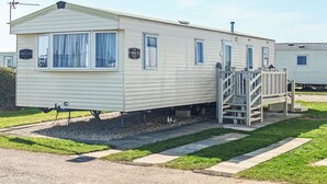 Une maison mobile dotée d’une rampe d’accès menant à l’entrée, d’un petit porche et d’une fenêtre avec un rideau.