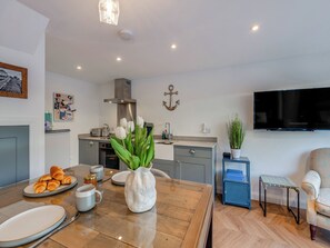 A modern kitchen with a dining area, a TV, and a potted plant.