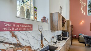 A modern kitchen with a marble countertop, wooden cabinets, a coffee station, and a view of the outdoors.