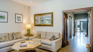 A living room with a sofa, coffee table, and a mirror. There are framed pictures on the wall and a door leading to a hallway.
