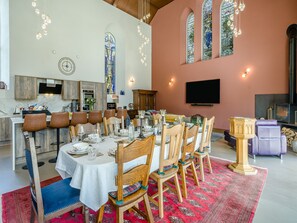 A dining area with a round table set for six, wooden chairs, a red patterned rug, and a kitchen in the background. - 5 bedroom accommodation in Duns (Duns)