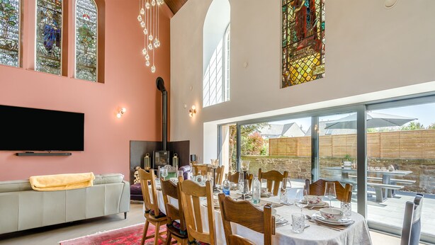 A dining area with a table set for six, wooden chairs, and a red patterned rug.