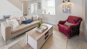 Ein Wohnzimmer mit einem beigefarbenen Sofa, einem roten Sessel, einem Couchtisch und einer Treppe.