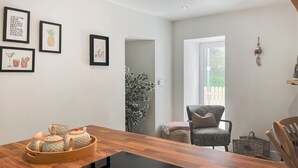 Ein modernes Wohnzimmer mit einem Holzesstisch, einem Couchtisch mit schwarzer Glasplatte und einer Sitzecke mit einem gemusterten Sessel und einem Korbwannenstuhl.