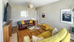 A living room with a brown leather sofa, yellow sofa, and a glass coffee table. There is a television on a wooden stand, a window with blinds, and a framed picture on the wall. - 2 bedroom accommodation in Canterbury (Canterbury)