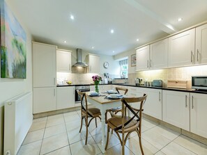 A modern kitchen with white cabinets, a central island with chairs, a stove, and a microwave.