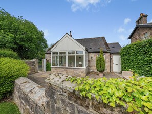 Une maison en pierre avec un toit à pignon, une véranda et un mur de pierre recouvert de lierre.