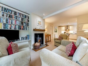 A living room with a fireplace, a bookshelf, a television, and a kitchen area.
