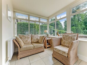 A sunlit room with wicker furniture, large windows, and a view of greenery.