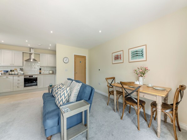 A modern kitchen with white cabinets, a built-in oven, and a dining area with a wooden table and chairs.