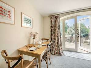 A dining area with a wooden table, chairs, a pitcher of flowers, a white teapot, and framed artwork on the wall.
