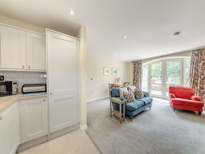 A modern kitchen with white cabinetry, a dining area with a blue sofa and red armchair, and a large sliding glass door leading to a garden.