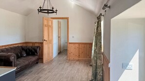 Un'ampia zona giorno con un divano in pelle marrone, pavimento in legno e un lampadario.