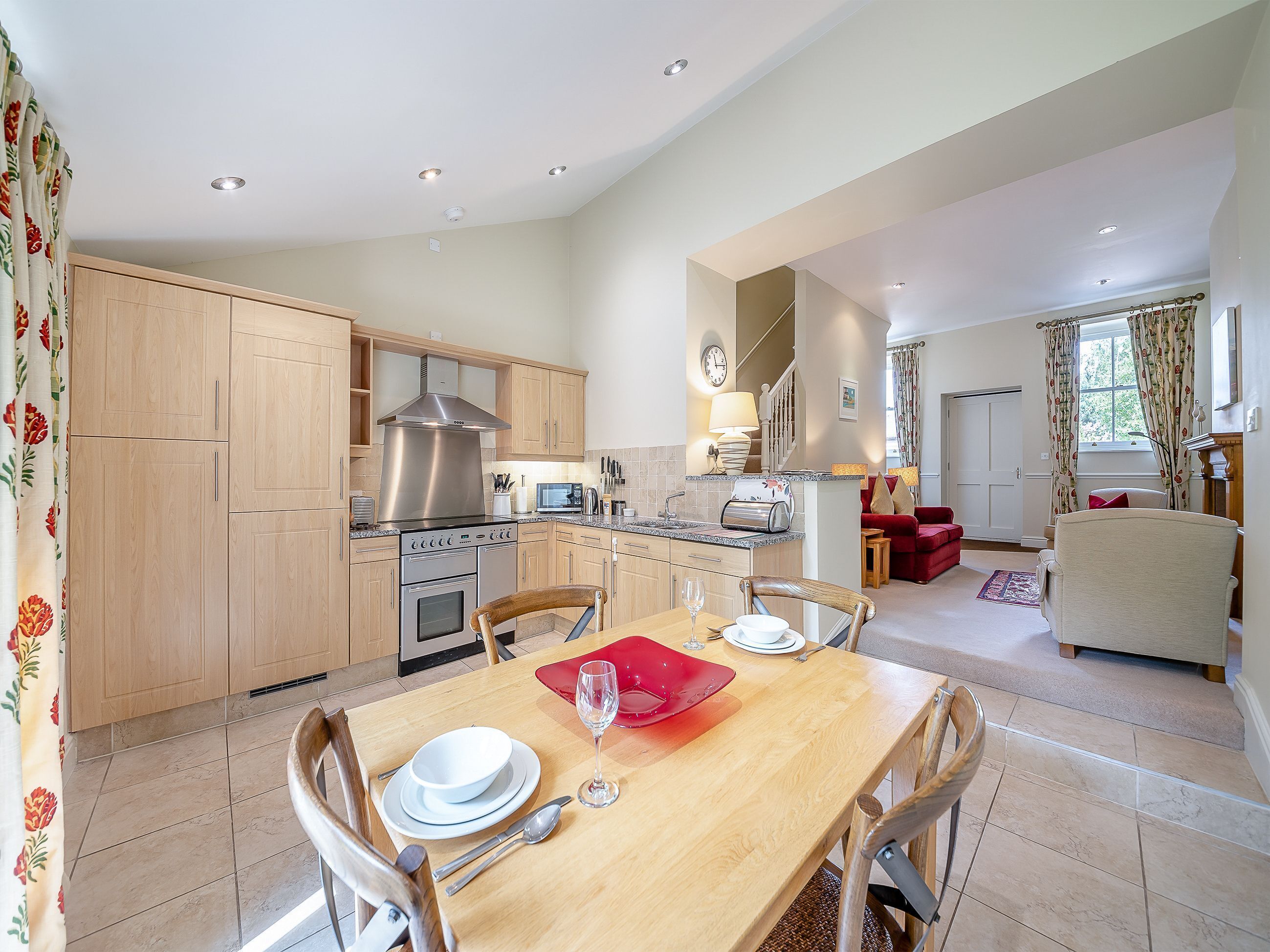 A modern kitchen with wooden cabinets, stainless steel appliances, and a dining area with a table set for two.
