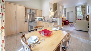 Une cuisine moderne avec des meubles en bois, des appareils électroménagers en acier inoxydable et un coin repas avec une table dressée pour deux personnes.