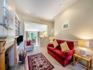 A living room with a fireplace, a red sofa, a bookshelf, and a dining area in the background.