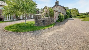Un bâtiment en pierre avec une allée de gravier, entouré de verdure et sous un ciel dégagé.