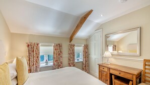 Une chambre à coucher avec un grand lit, un bureau en bois, une chaise, un miroir et une fenêtre avec des rideaux.