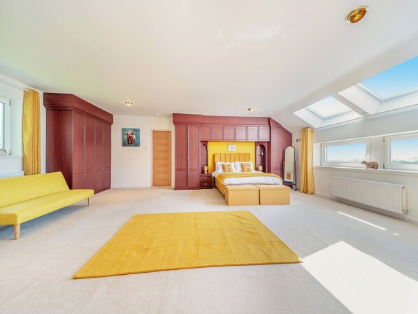 Une chambre spacieuse avec un grand lit, un canapé jaune et une vue sur le ciel grâce à la lucarne.
