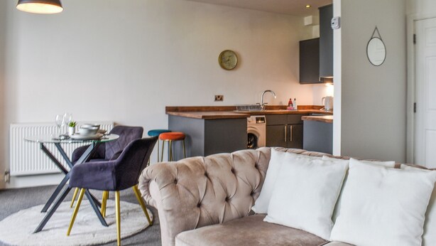 Una sala de estar moderna con un sofá color beige, una mesa de comedor con sillas y una cocina al fondo.