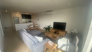 Een moderne woonkamer met een grijze bank, een tv-meubel en een eethoek met een tafel en stoelen.