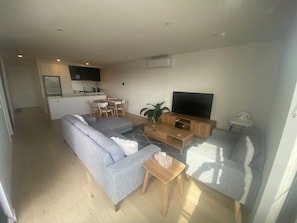 Ein modernes Wohnzimmer mit grauem Sofa, einem TV-Schrank und einem Essbereich mit Tisch und Stühlen.